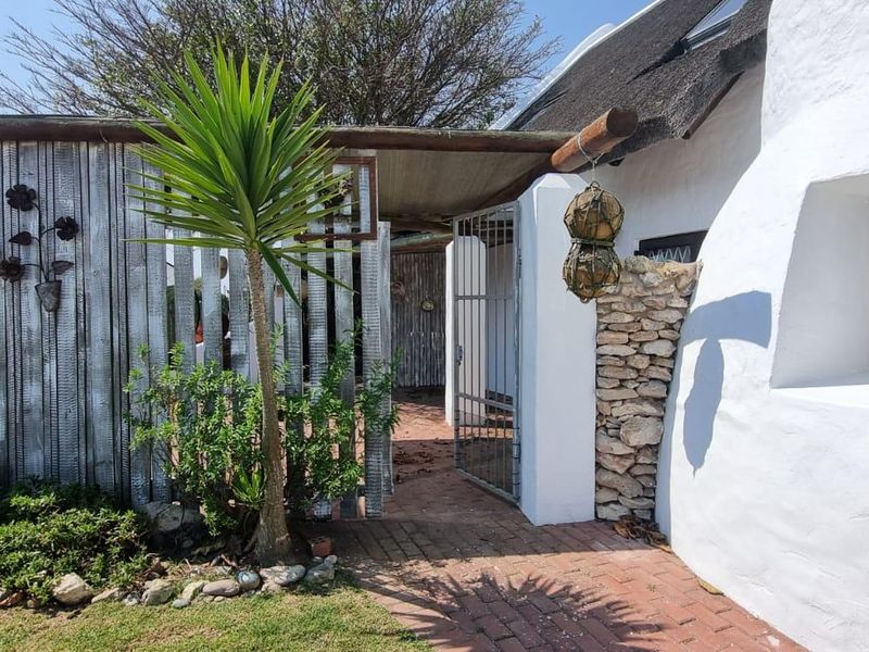 A charming entrance area featuring a thatched roof, stone accents, and a timber pergola leading to a secure gated walkway.