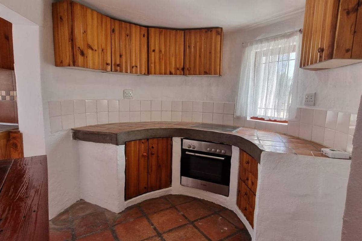 A rustic kitchen featuring built-in wooden cabinetry, tiled countertops, and a built-in oven with an electric hob.