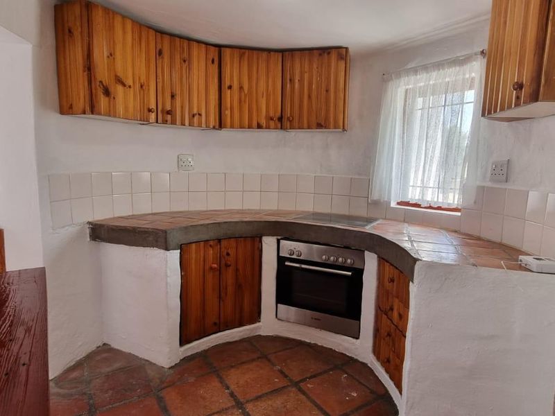 A rustic kitchen featuring built-in wooden cabinetry, tiled countertops, and a built-in oven with an electric hob.