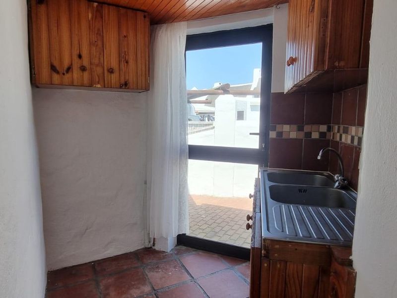 A compact scullery area featuring timber cabinetry, a double stainless steel sink, and direct access to an outdoor patio space.