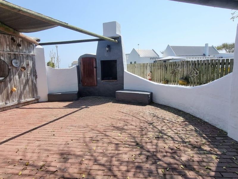 Outdoor patio area featuring a built-in braai, brick paving, and a timber privacy screen, offering a functional space for outdoor entertaining.