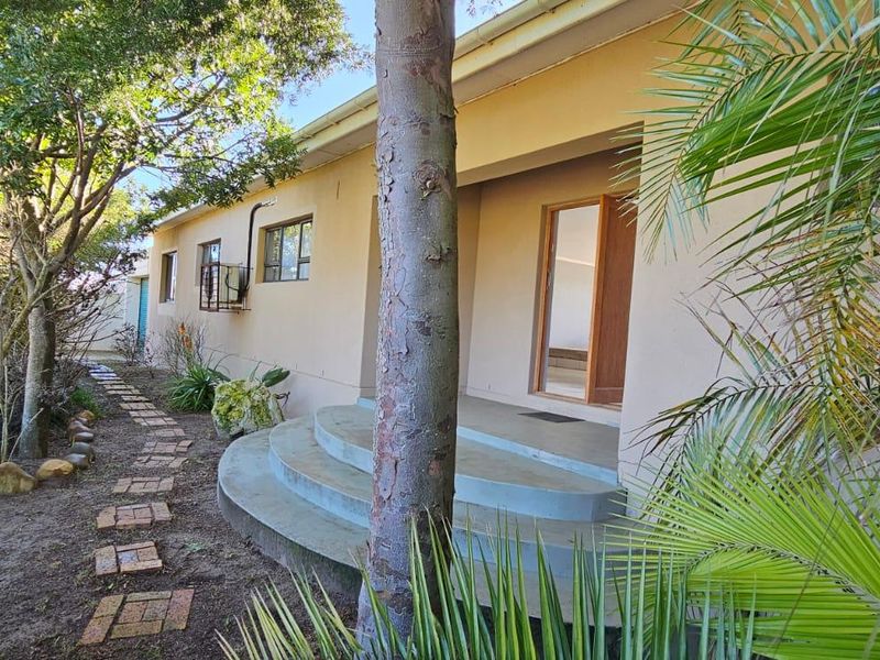 Rear exterior view of the property featuring a concrete staircase leading to a sliding door entrance, surrounded by a garden and brick pathway.