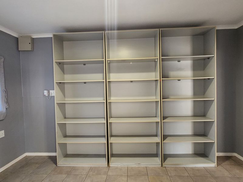 An empty living area featuring extensive built-in shelving units, tiled flooring, and grey painted walls, providing a functional storage space.