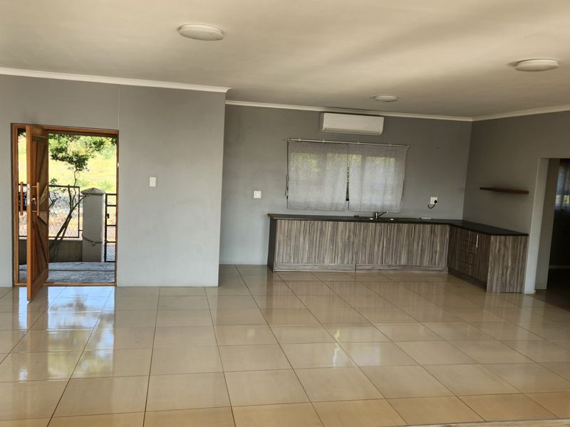 Spacious open-plan living area featuring neutral tiled flooring, built-in kitchen cabinetry with a sink, and an integrated air conditioning unit.