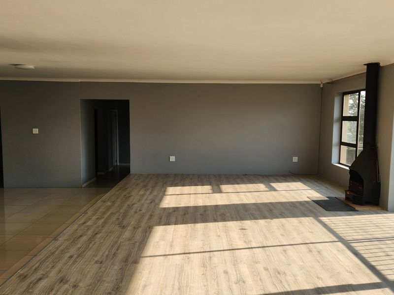 Spacious open-plan living area featuring modern laminate and tiled flooring, a built-in wood-burning fireplace, and large windows providing ample natural light.