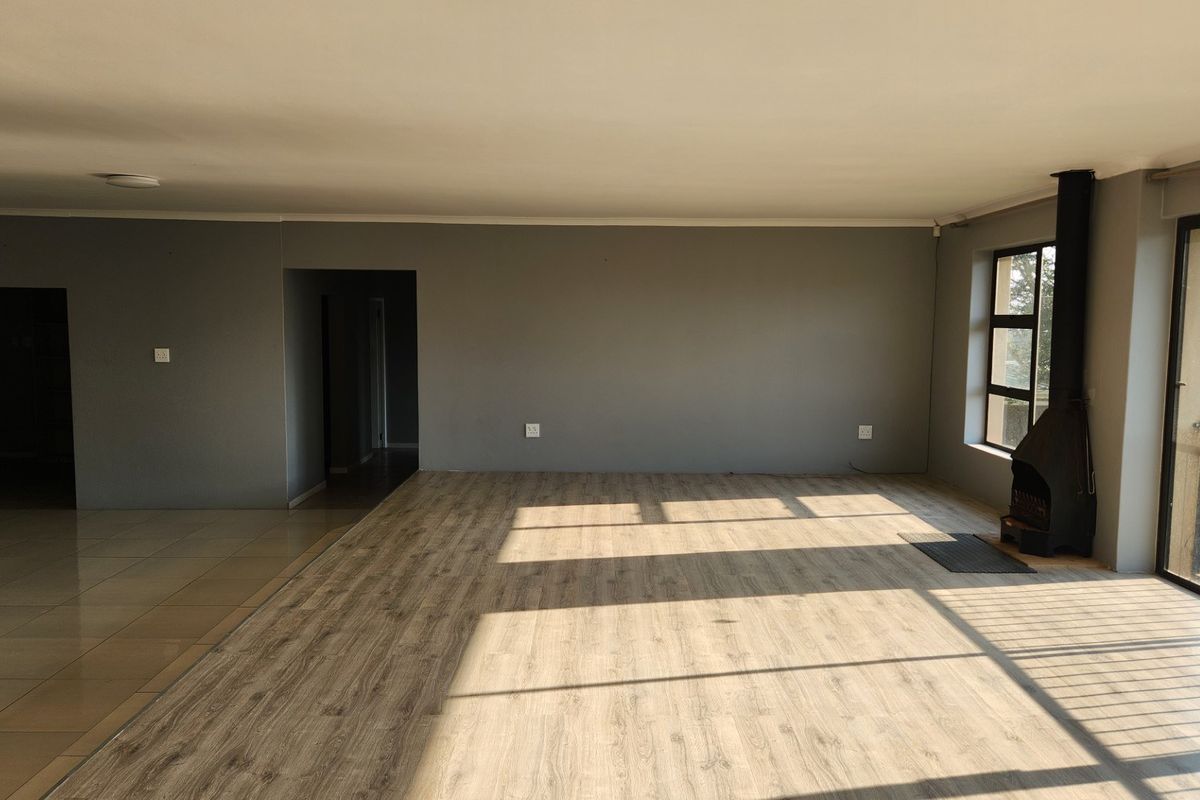 Spacious open-plan living area featuring modern laminate and tiled flooring, a built-in wood-burning fireplace, and large windows providing ample natural light.