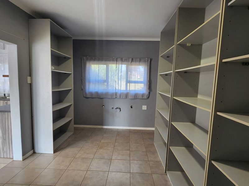 A functional scullery or utility space featuring built-in shelving, tiled flooring, and visible plumbing connections ready for appliance installation.