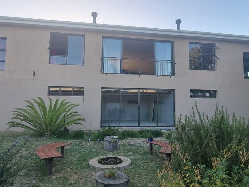 Rear view of a two-story residential property featuring a balcony, large sliding glass doors, and a garden area with a fire pit.