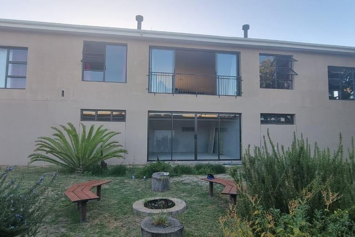 Rear view of a two-story residential property featuring a balcony, large sliding glass doors, and a garden area with a fire pit.