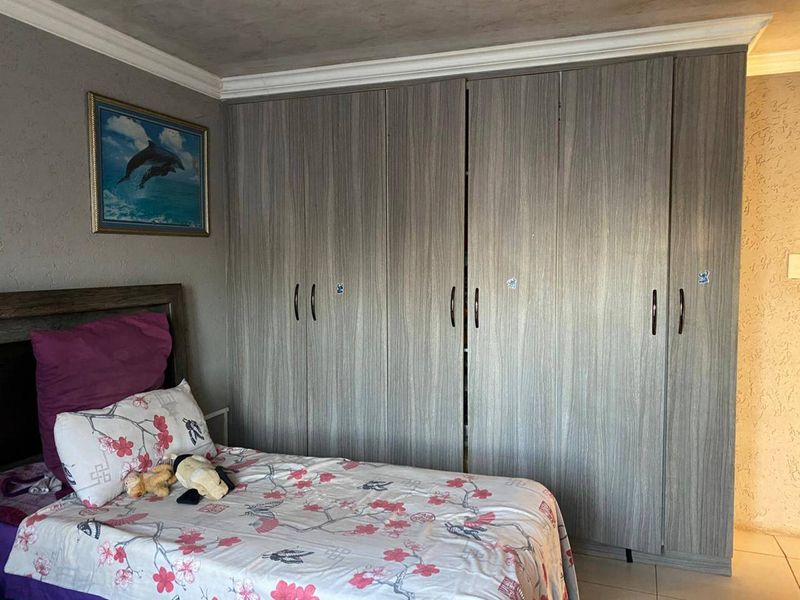 A bedroom featuring modern wood-grain built-in cupboards, crown molding, and tiled flooring.