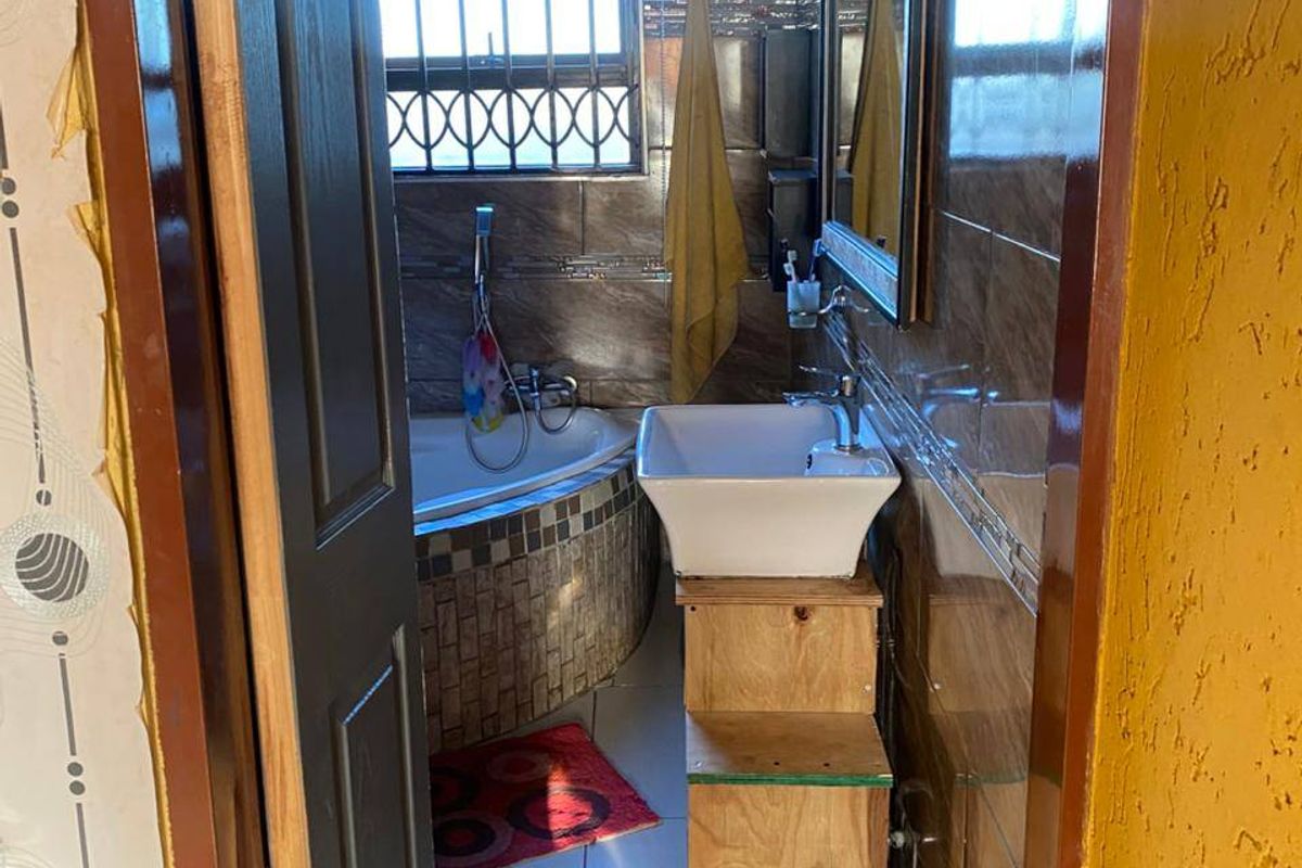 A compact bathroom featuring a corner bathtub, tiled walls, and a vessel sink with an unfinished wooden vanity base.