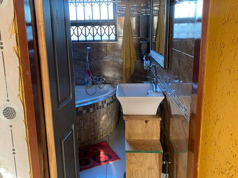 A compact bathroom featuring a corner bathtub, tiled walls, and a vessel sink with an unfinished wooden vanity base.