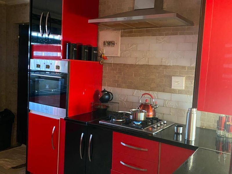 Modern kitchen featuring high-gloss red and black cabinetry, granite countertops, a built-in oven, gas hob, and a stainless steel extractor fan.