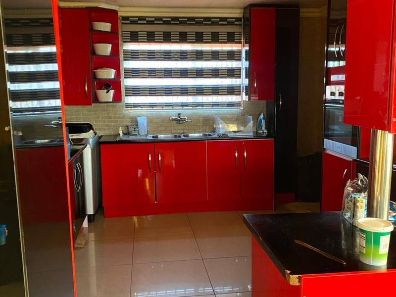 A kitchen featuring high-gloss red cabinetry, a double bowl stainless steel sink, tiled backsplash, and polished floor tiles.