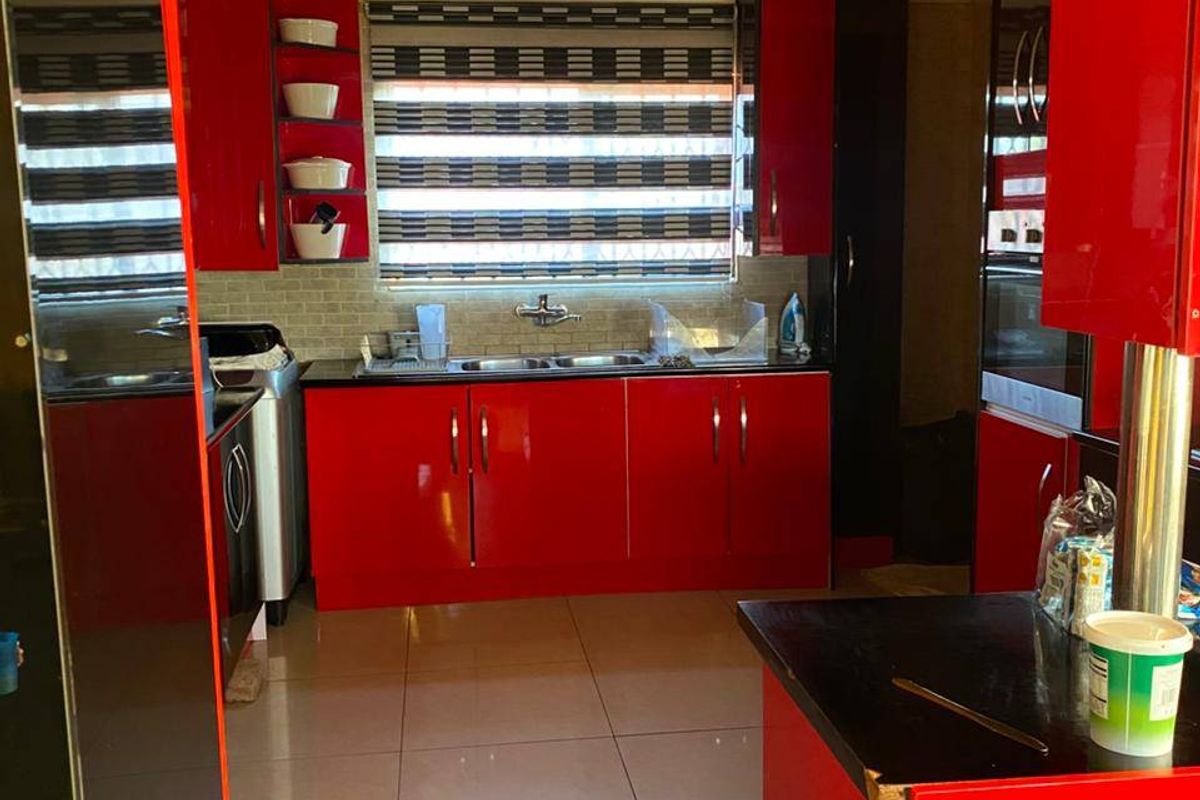 A kitchen featuring high-gloss red cabinetry, a double bowl stainless steel sink, tiled backsplash, and polished floor tiles.