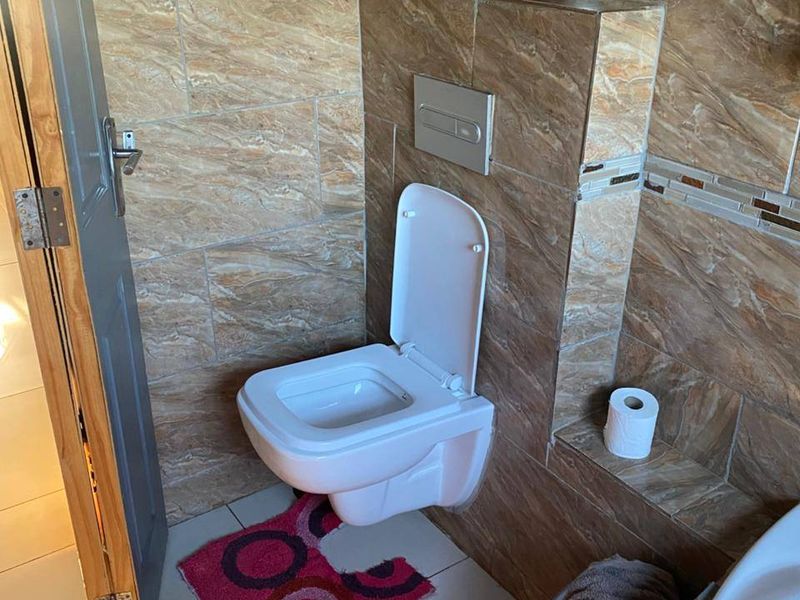 A modern bathroom featuring a wall-mounted toilet with a concealed cistern and full-height decorative wall tiling.