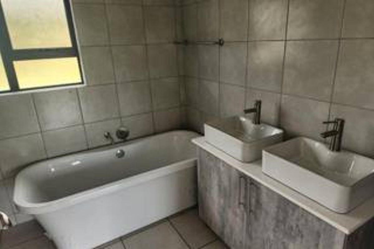 Modern bathroom featuring a freestanding bathtub, double vanity with vessel sinks, and neutral wall tiling.