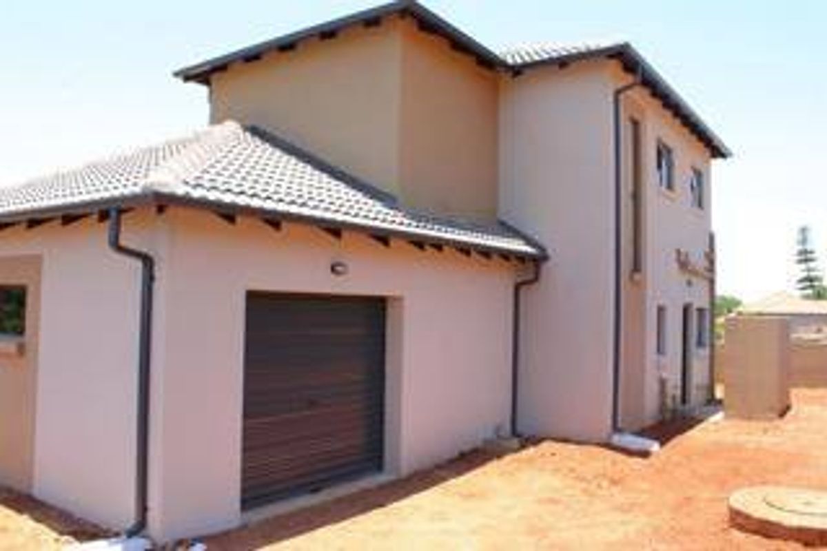 Rear view of a double-story residential house featuring a single garage, tiled roof, and plastered exterior walls with unfinished surrounding ground.