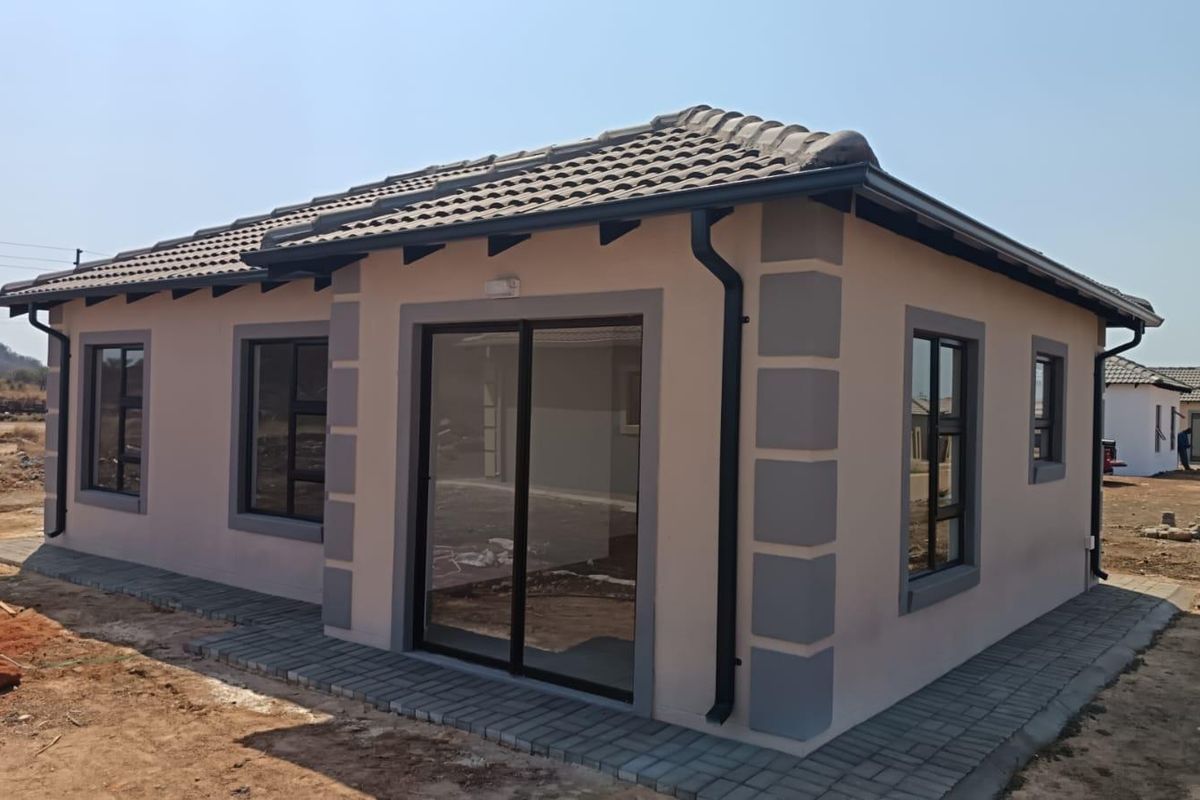 A modern single-story house exterior featuring a tiled roof, aluminium window frames, and a sliding glass door with surrounding paved walkway.