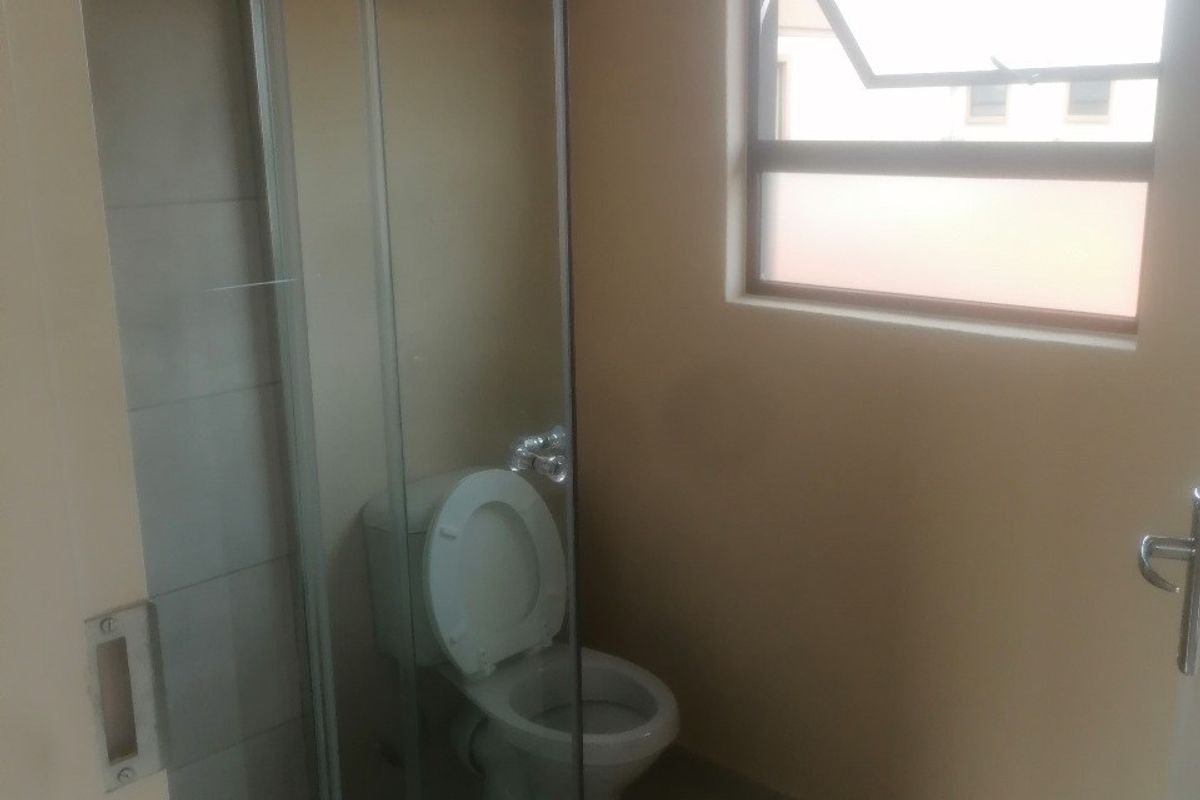 A functional bathroom featuring a glass shower enclosure, a standard toilet, and tiled flooring with natural light from a top-hung window.
