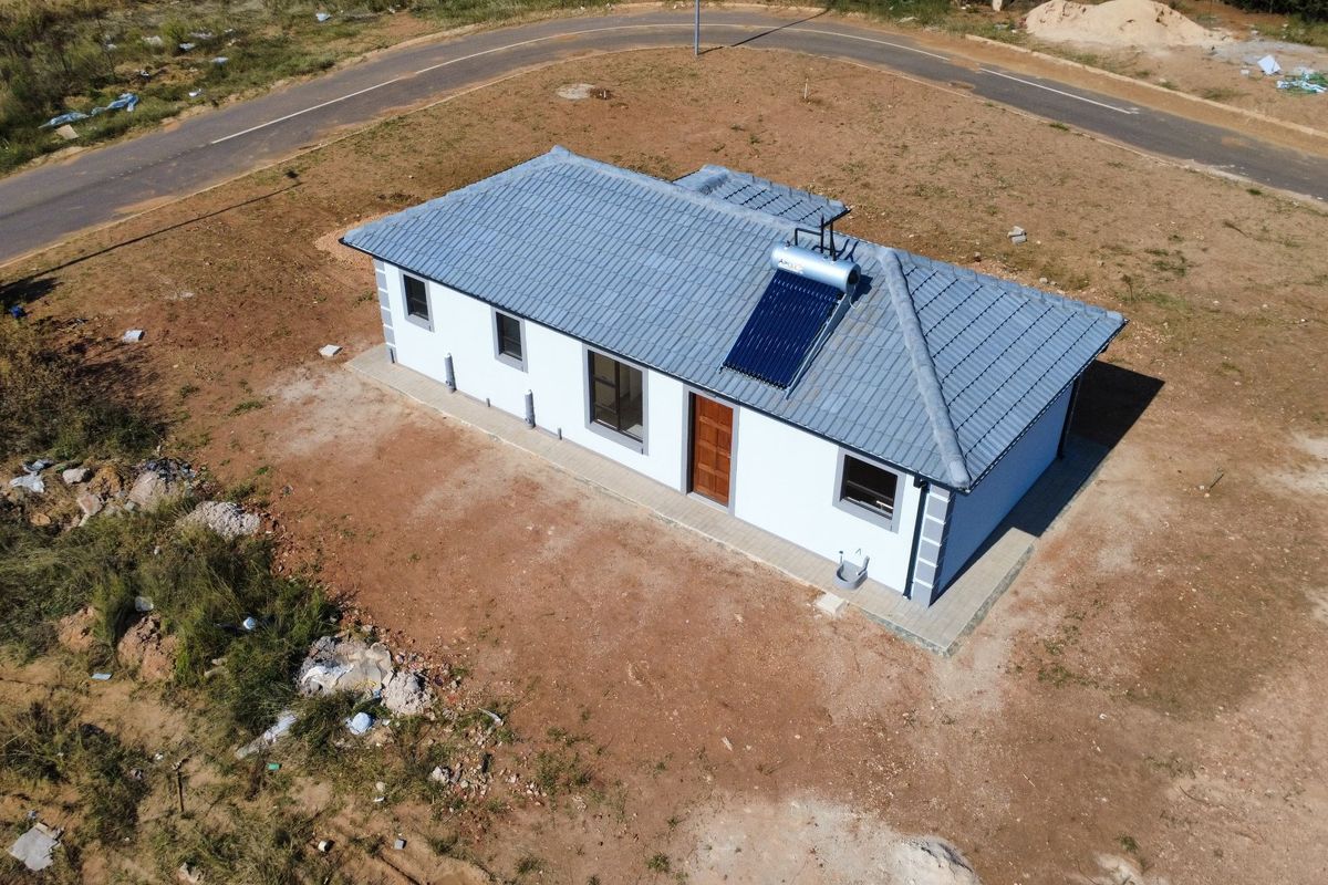 Aerial view of a detached single-story house featuring a tiled roof, solar water heating system, and surrounding undeveloped land.