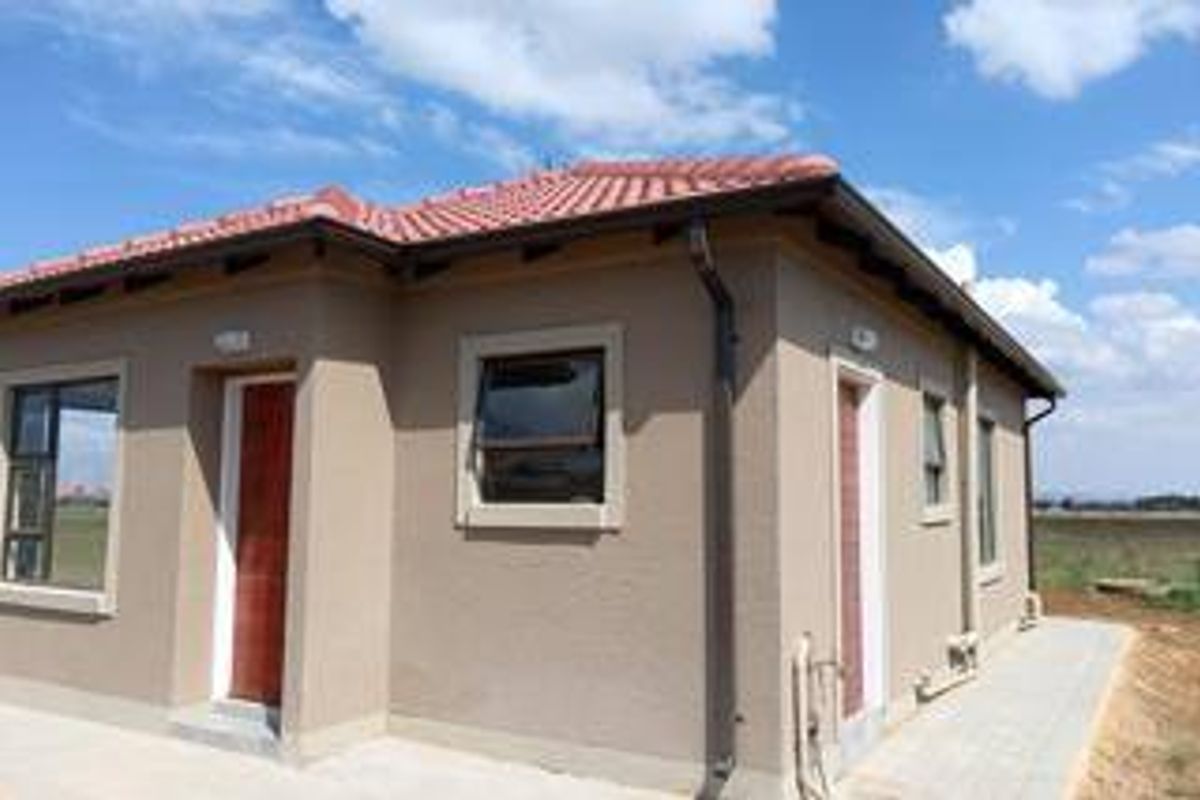 A view of the rear exterior of the house featuring plastered walls, a tiled roof, and paved walkways.