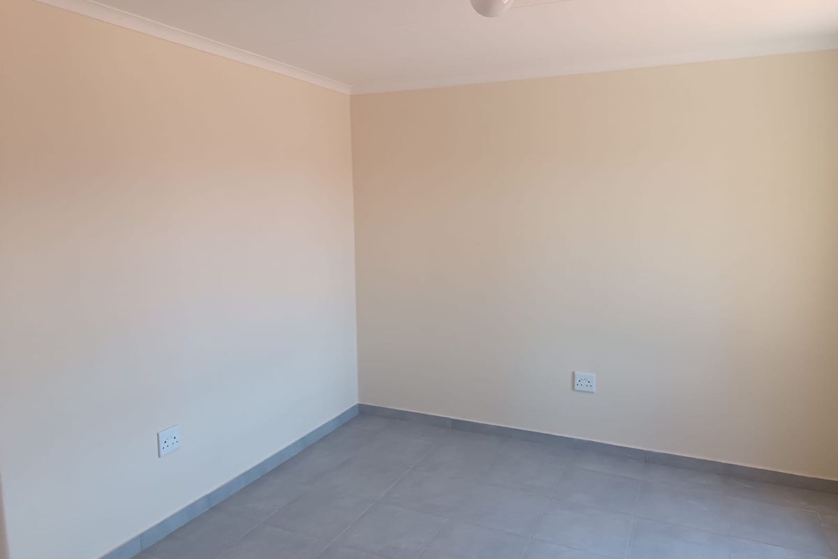 A clean, empty bedroom featuring neutral painted walls, grey floor tiles, and standard electrical fixtures.