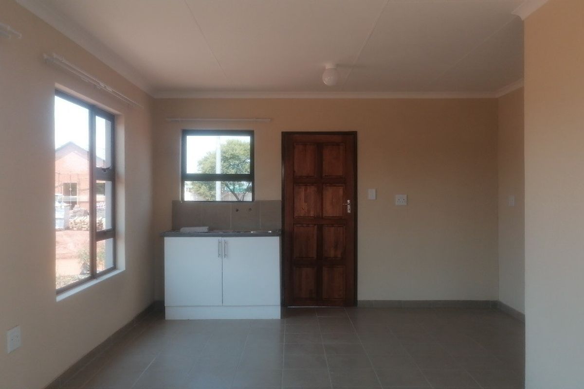 A compact, empty kitchen area featuring a single sink cabinet, tiled backsplash, ceramic flooring, and a solid timber door.