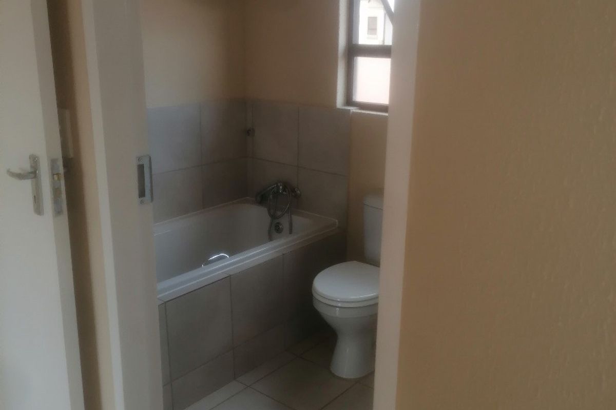 A functional bathroom featuring a bathtub, toilet, and neutral tiled finishes, viewed through a doorway.