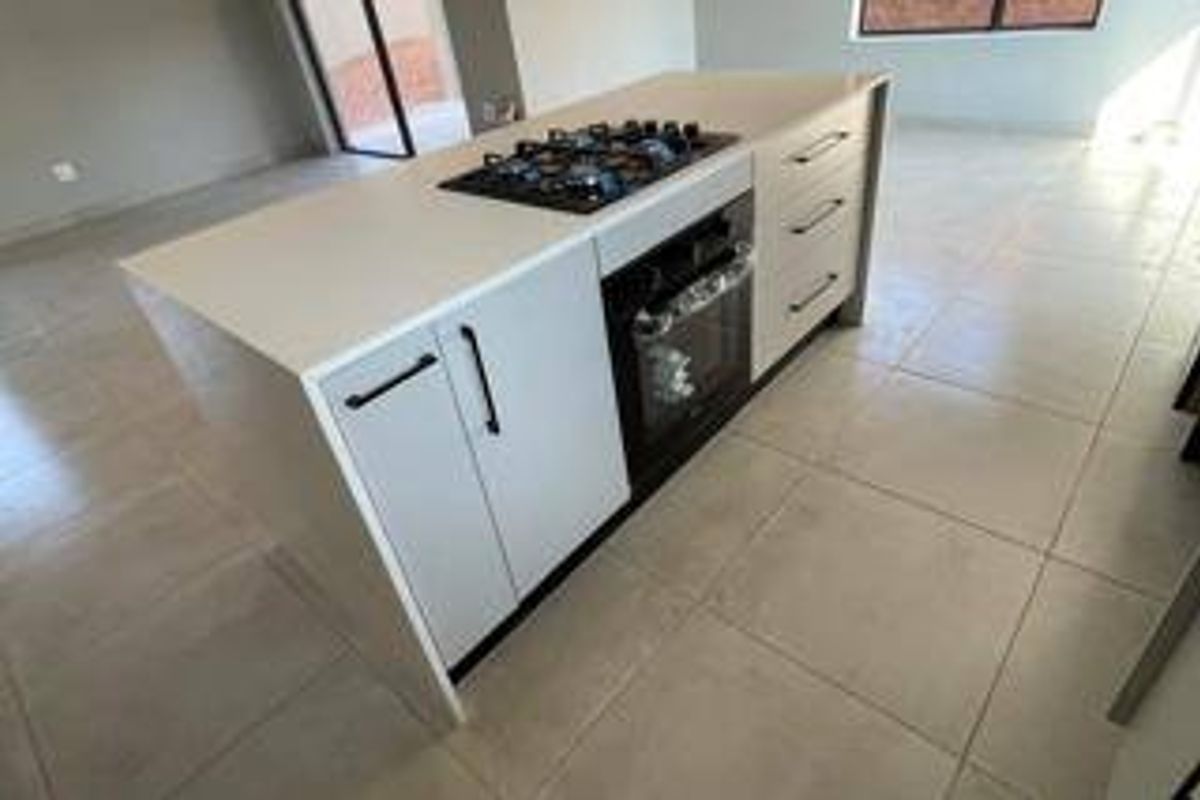 Modern kitchen island featuring a built-in gas hob, oven, and stone countertop, set within an open-plan living space with neutral tiled flooring.