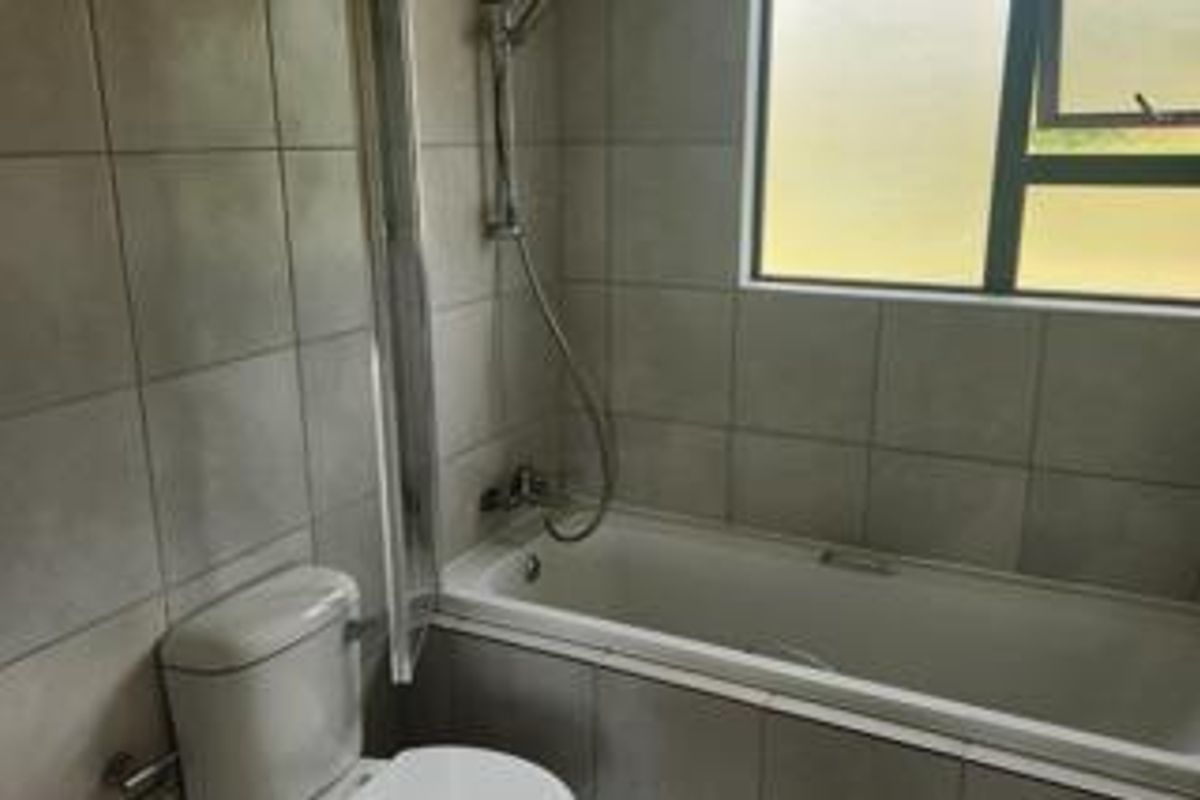 A functional bathroom featuring a bathtub with an integrated shower, tiled walls, and a frosted window for privacy.