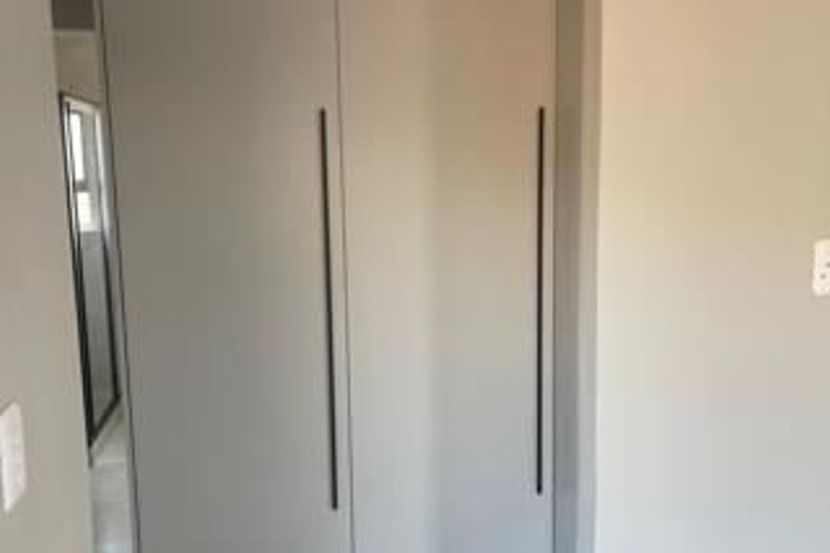 A bedroom interior featuring modern built-in cupboards with sleek vertical handles.