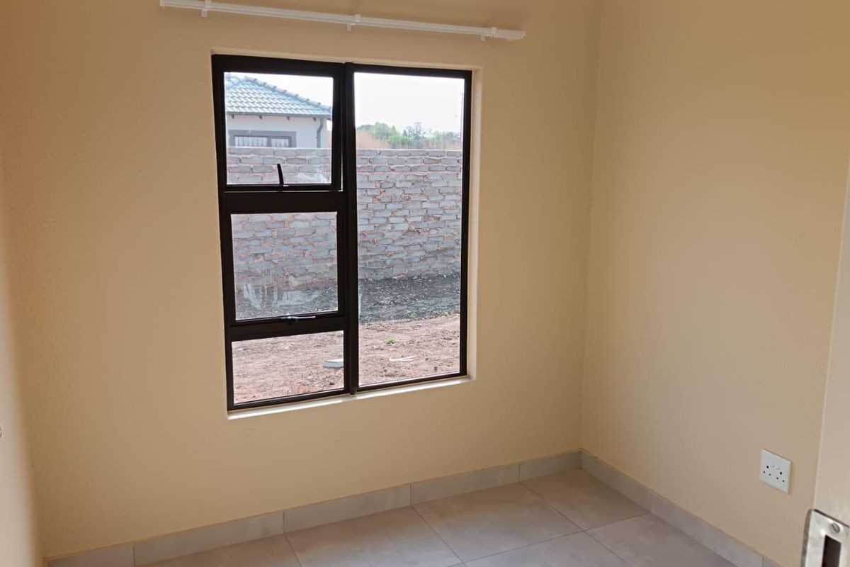 A clean, empty bedroom featuring neutral wall paint, tiled flooring, and a modern aluminium-framed window.