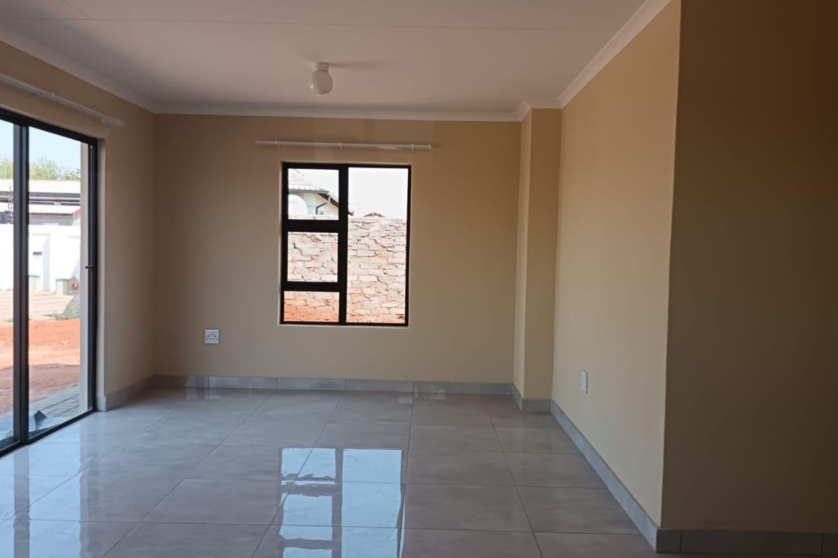 A bright, empty living room featuring neutral walls, large format floor tiles, and a sliding glass door providing access to the exterior.