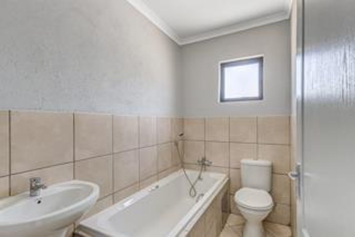 A functional bathroom featuring a pedestal basin, bathtub, and toilet with neutral wall and floor tiling.