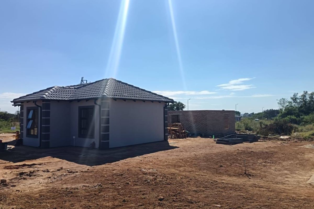 Rear view of a modern house with tiled roof and aluminium windows, set on a large, undeveloped plot of land.