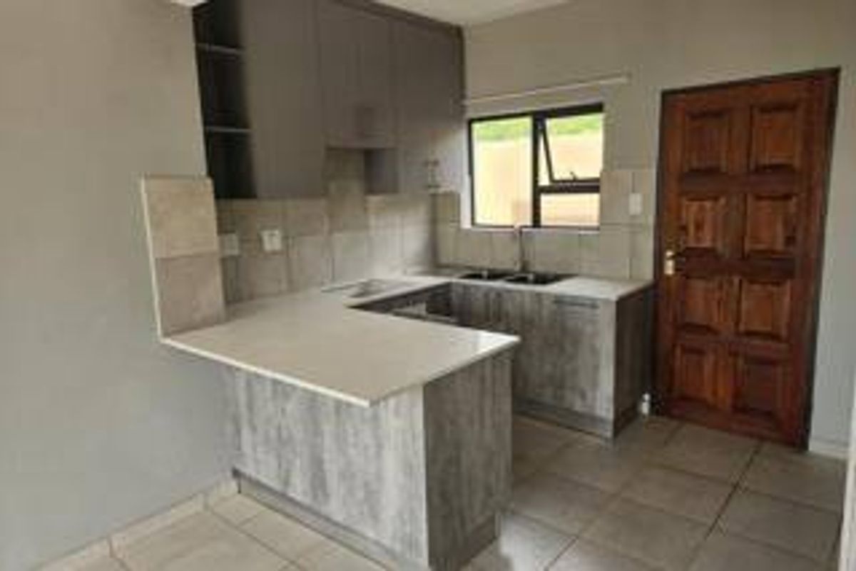 A functional kitchen featuring modern grey cabinetry, stone countertops, a double sink, and tiled flooring, offering a clean and practical workspace.