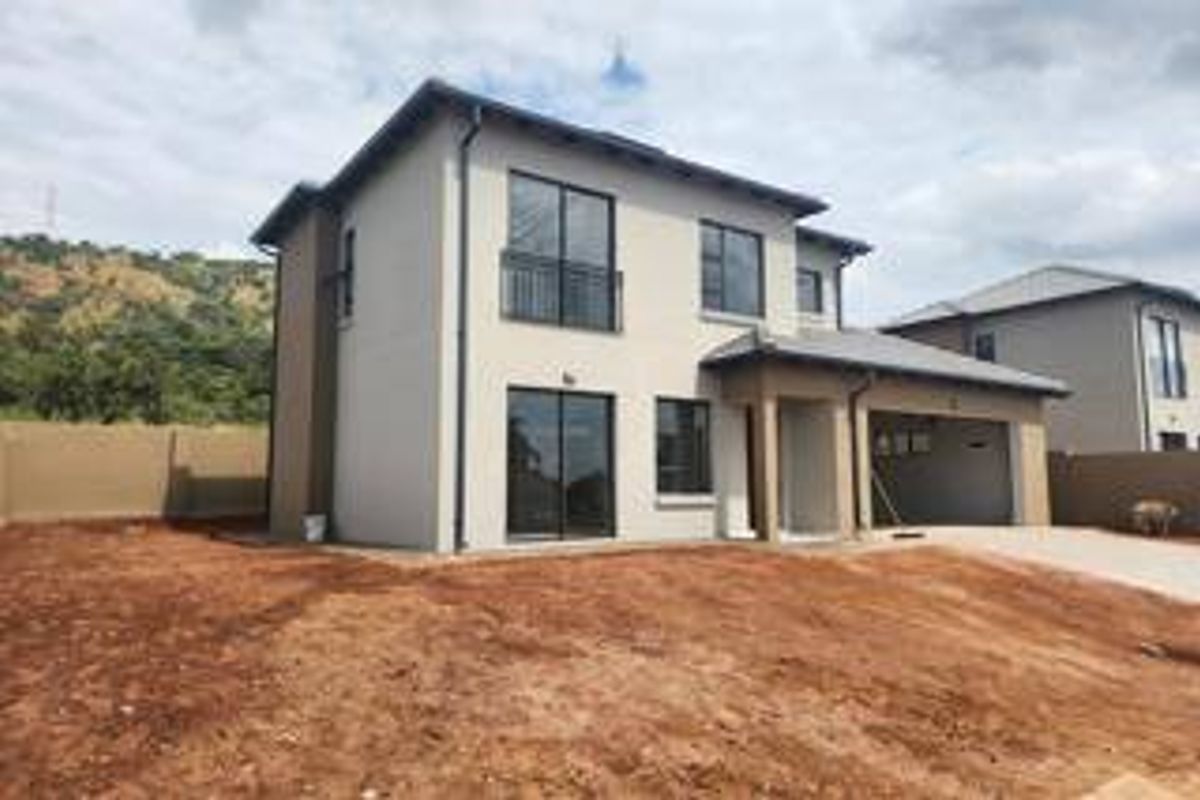 Rear view of a modern double-story house featuring a balcony, sliding doors, attached garage, and an unlandscaped garden area.