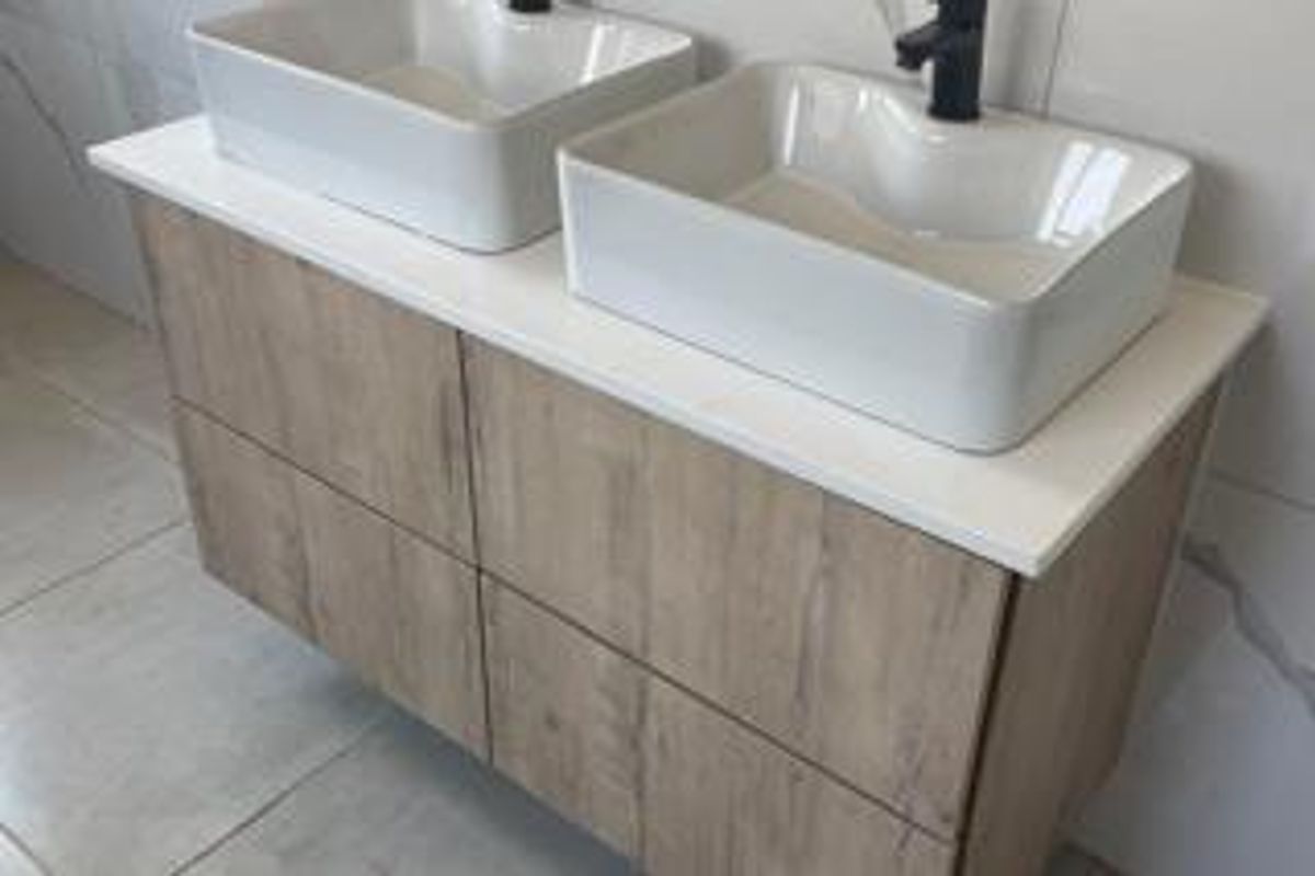 Modern bathroom vanity featuring a double vessel sink setup with contemporary wall-mounted faucets and wood-grain cabinetry.