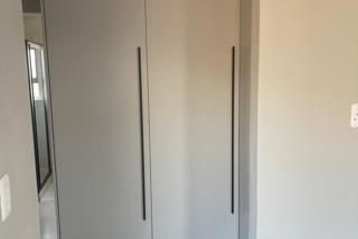 A bedroom interior featuring modern, neutral-toned built-in cupboards with sleek vertical handles.