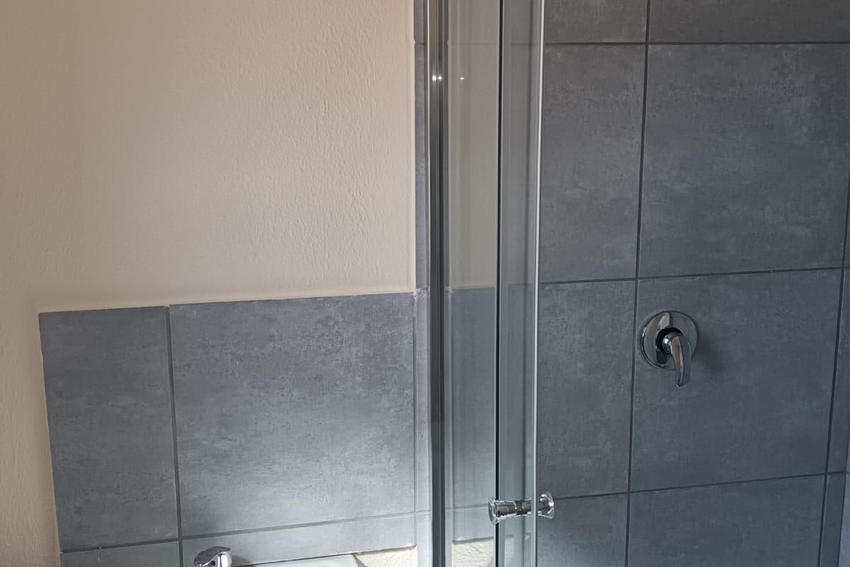 A clean, modern bathroom featuring a pedestal basin and a glass-enclosed shower with grey tiled walls.