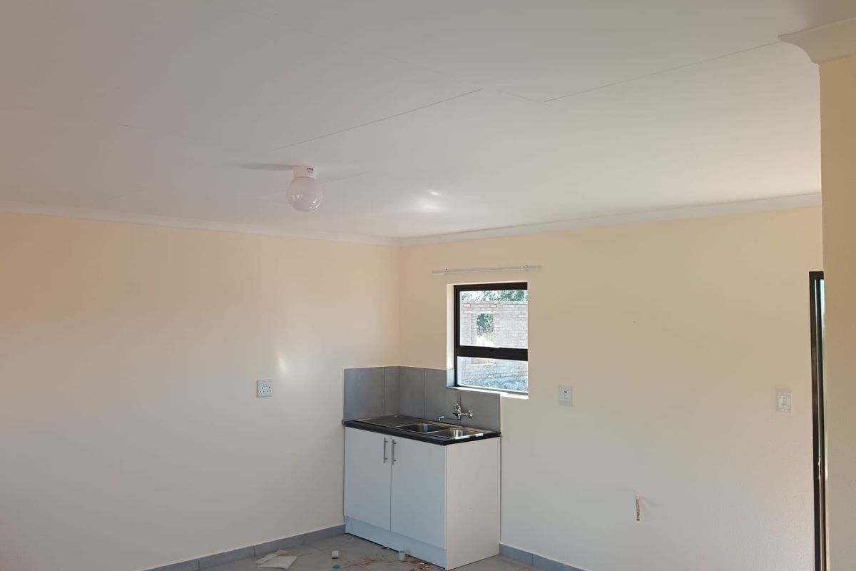 A compact, empty kitchen area featuring basic base cabinetry, a stainless steel sink, tiled splashback, and tiled flooring in a neutral interior space.