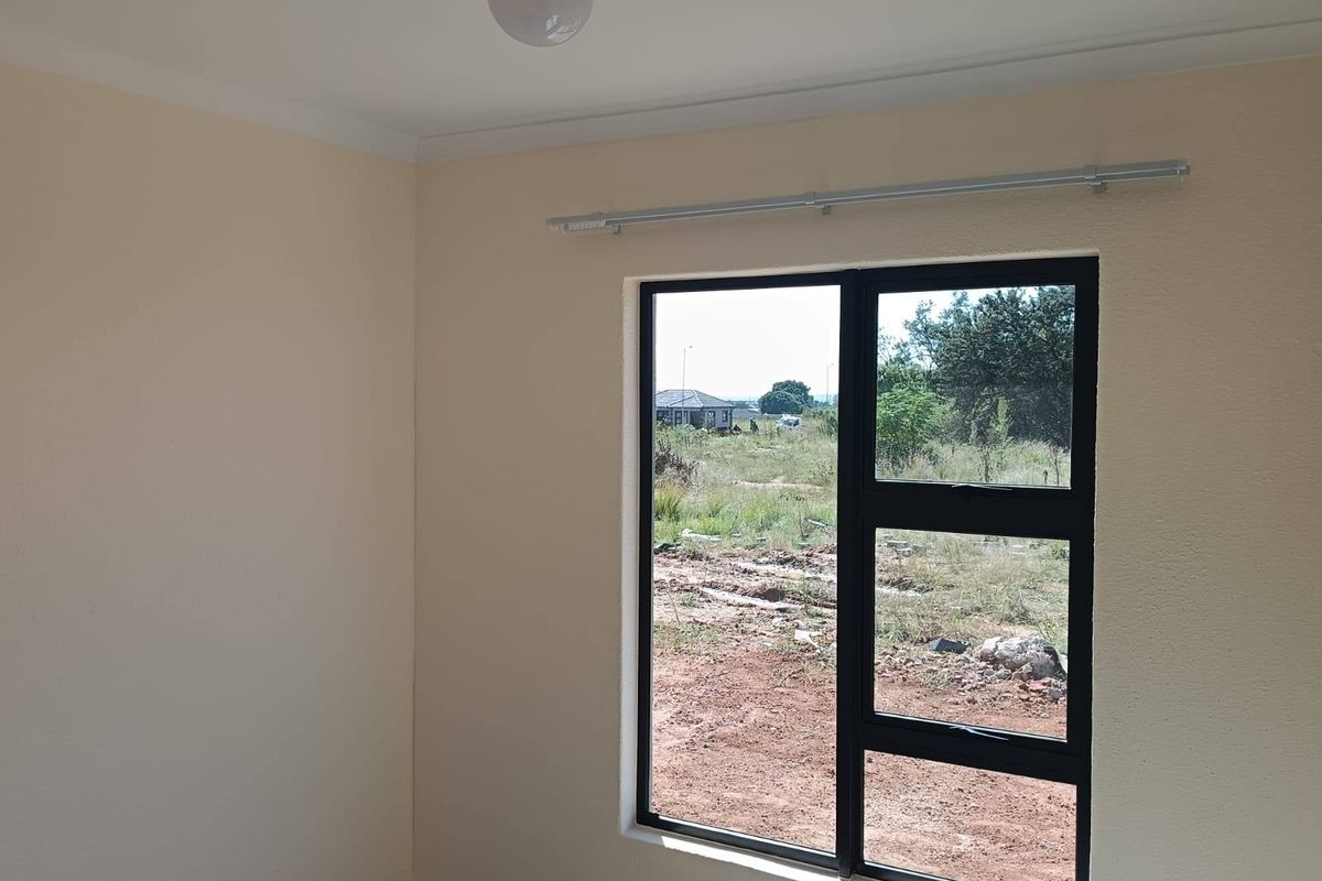 A clean, empty bedroom featuring neutral walls, a modern black aluminium window frame, and a fitted curtain rod.