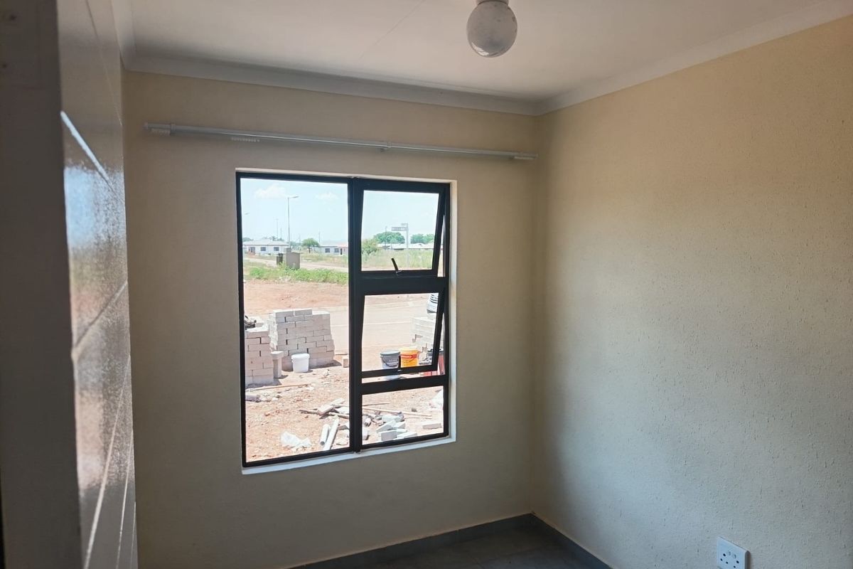A clean, empty bedroom featuring tiled flooring, neutral walls, and an aluminium-framed window with a curtain rail installed.
