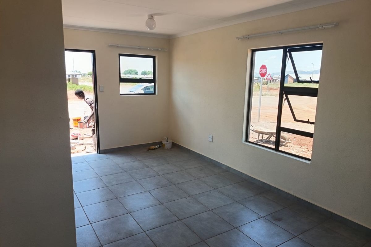 An empty, well-lit living area featuring neutral tiled flooring, modern aluminium window frames, and clean wall finishes, ready for personalization.