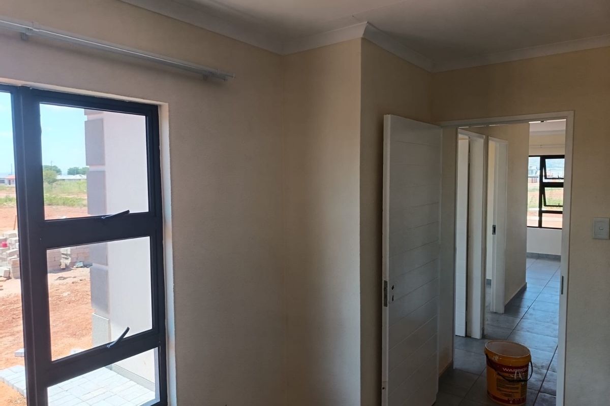 A bright, empty bedroom featuring tiled flooring, neutral walls, and modern aluminium window frames, offering a clean canvas for interior design.