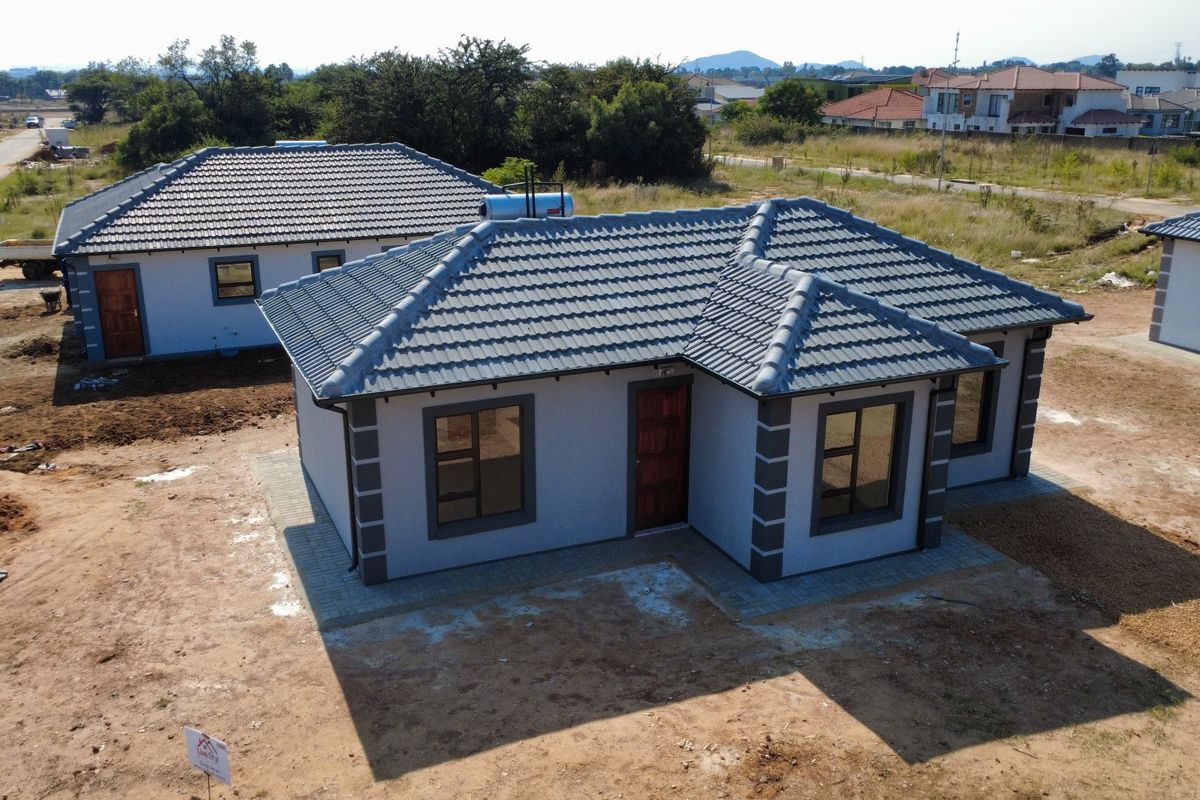 Aerial view of a modern detached house featuring a tiled roof, solar geyser, and paved perimeter in a developing residential area.