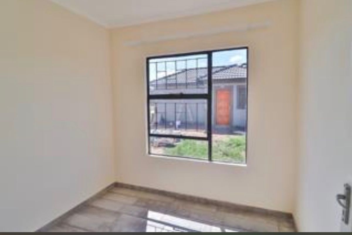 A clean, empty bedroom featuring tiled flooring, a large window with security burglar bars, and a neutral paint finish.