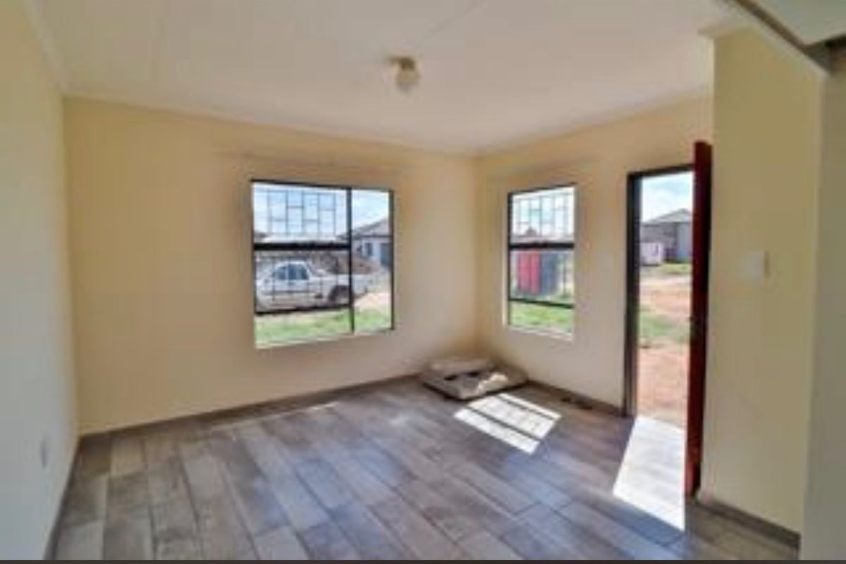 A bright, empty living area featuring modern wood-look floor tiles, security-barred windows, and direct access to the exterior.