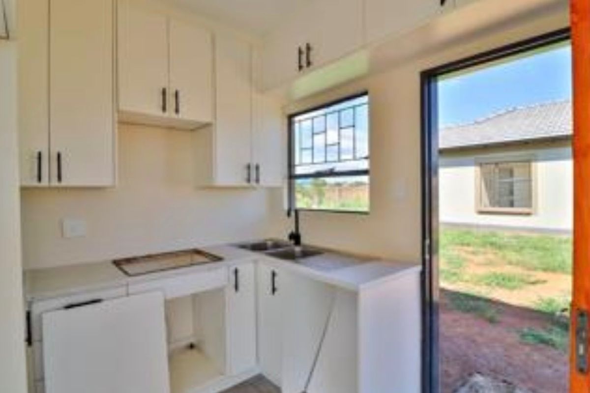 A compact kitchen area featuring white cabinetry, a stainless steel sink, and direct access to the rear yard through a sliding door.